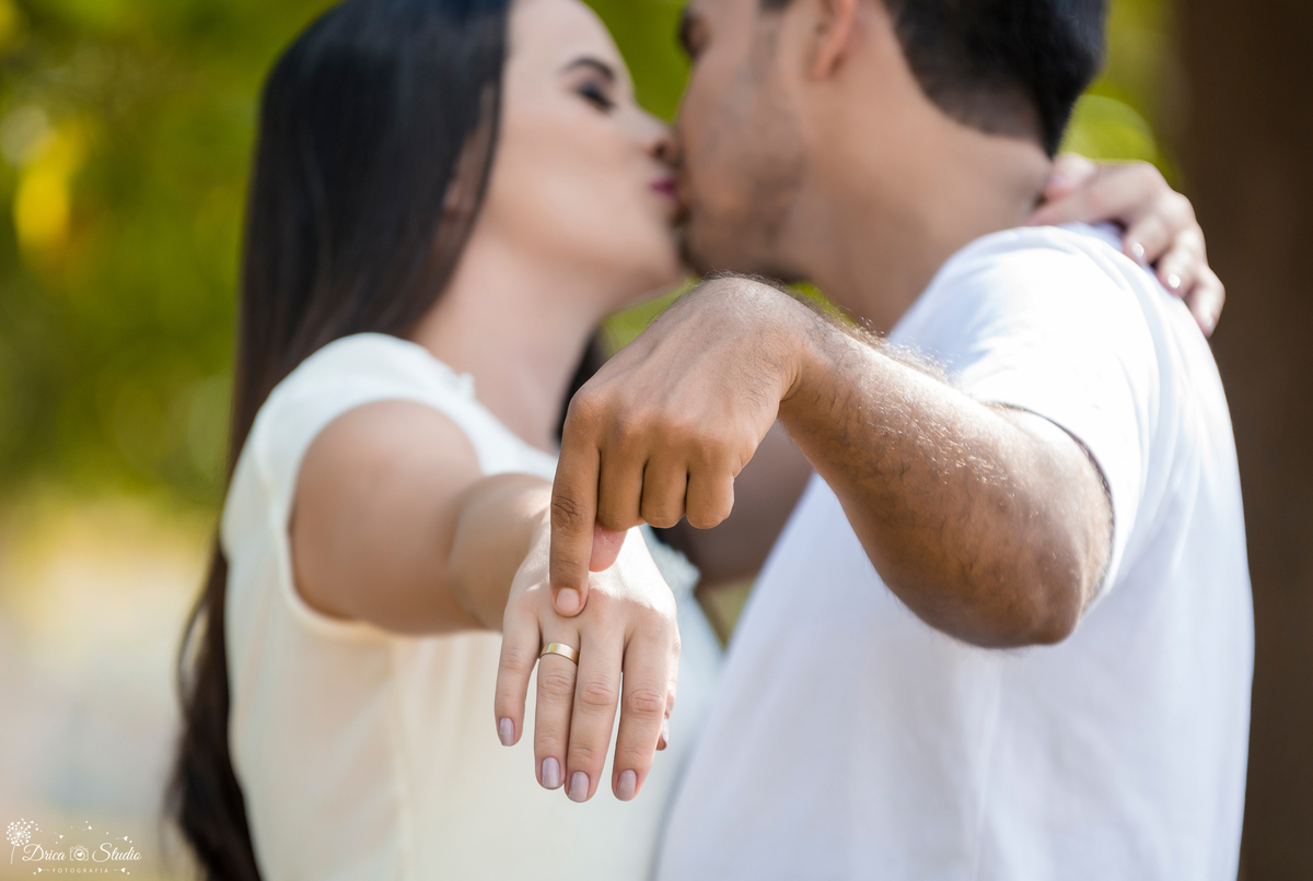 ensaio externo de noivos se beijando e apontando para as alianças os noivos estão de branco em uma paisagem verde.Drica Studio- Fotografias- Fotografo- Casamento- Xinguara – Pará- Fotografa-Casal- Pre Wedding- Família- Nova Canadá- ensaio- Externo.