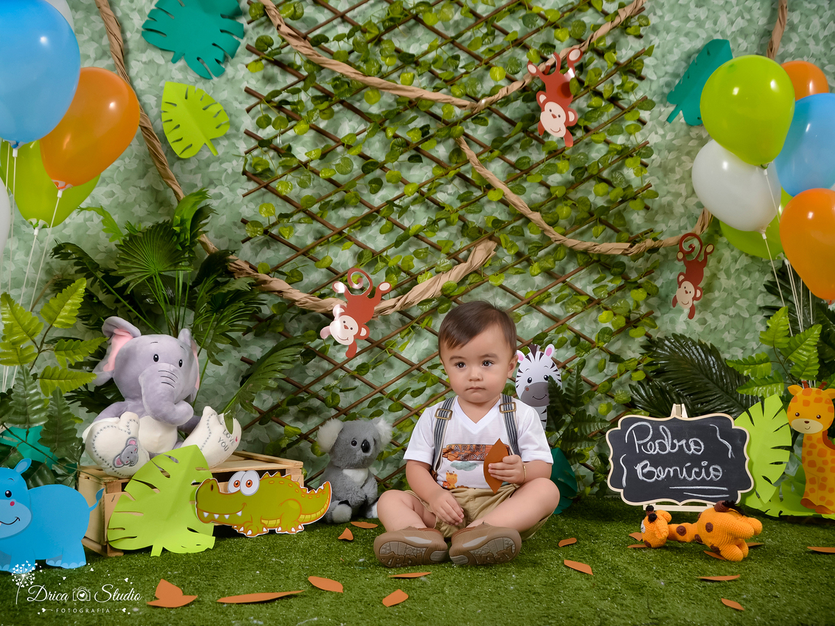 ensaio infantil Smash no tema safári, onde tem uma criança sentada rodeado de bruxinhos e balões, e tem uma lousa com seu no,e escrito ao lado dele. Drica Studio Fotografias-Fotógrafa Infantil- Fotógrafo em Xinguara-Fotógrafo de Criança- Ensaio Infantil.