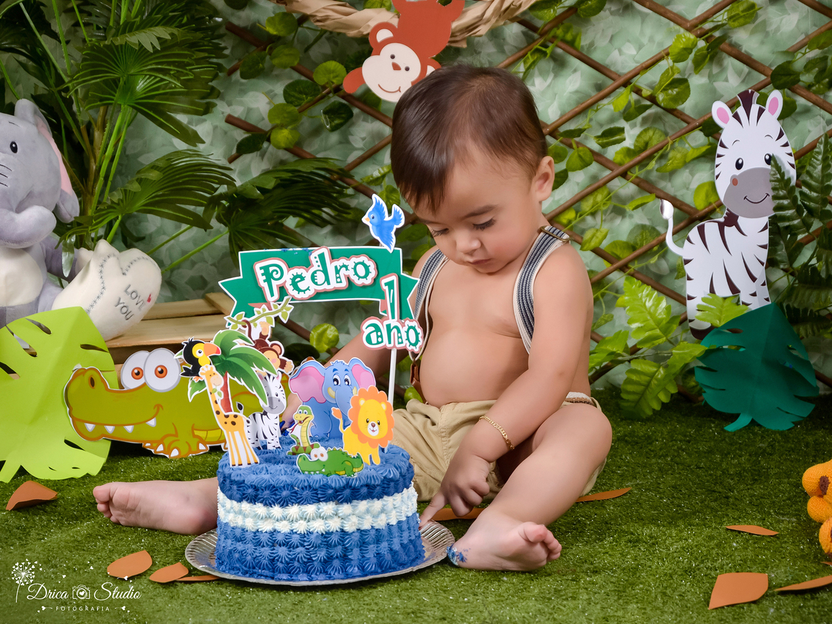 fotografia de uma criança em um cenário Smash no tema safári com o bolo entre suas pernas ele esta catando com o dedinho um pedacinho que caiu. Drica Studio fotografia estúdio de  acompanhamento.  Fotógrafa Infantil- Fotógrafo em Xinguara-Fotógrafo bebê.