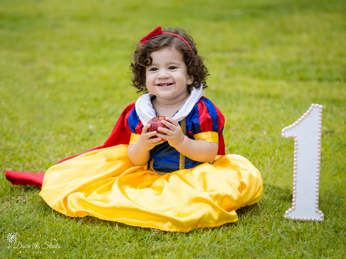  Smash the Cake-Branca de Neve- sorrindo-com a maçã-sentada na grama-Xinguara- Pará- ensaio infantil- ensaio externo- ensaio de família- contos de fada- bolo- amarelo- Fotógrafa- Drica Studio- Fotografia de família.