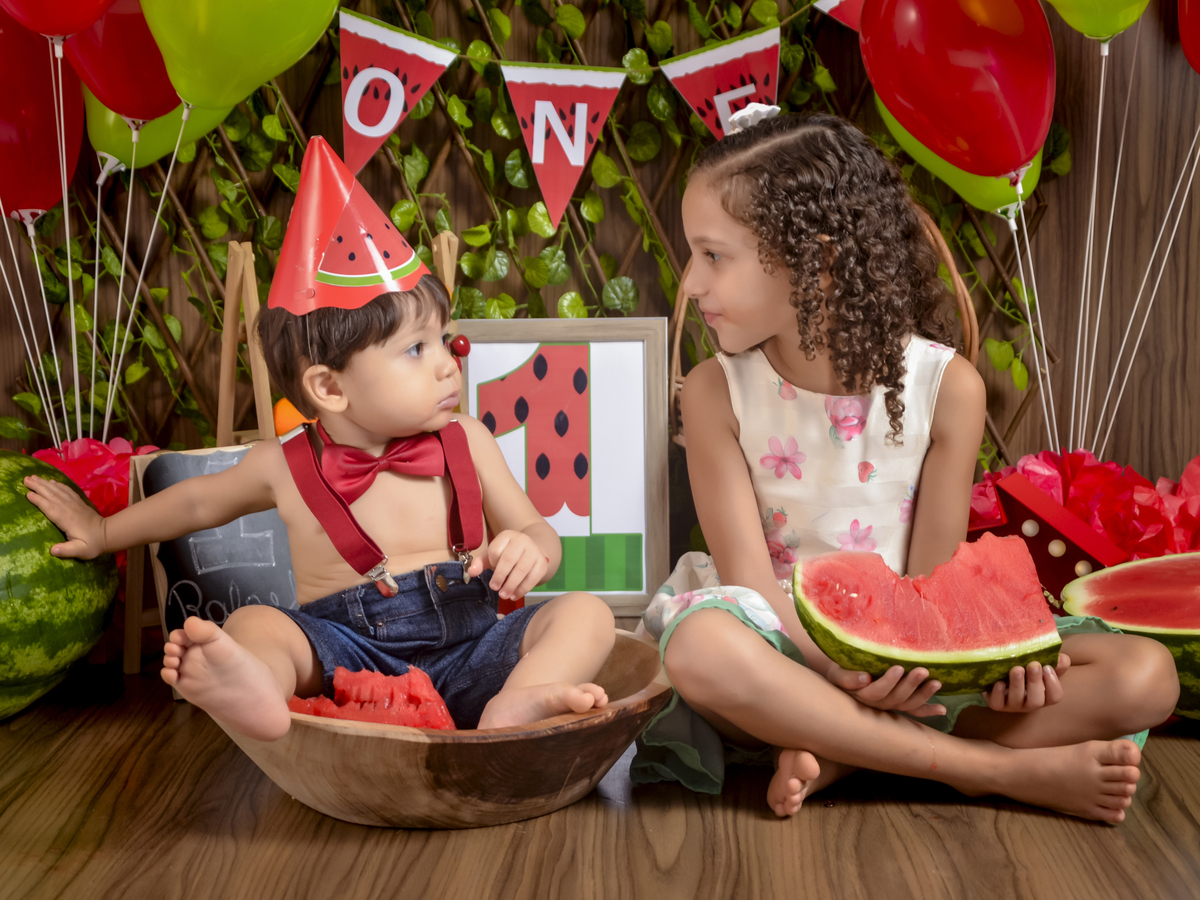 sentado na gamela olhando p/ irmã-Smash the Fruit-fruta-melancia-suspensório vermelho-gravata borboleta-ensaio infantil-gamela-crianças-book-acompanhamento mensal-Kids-foto em estúdio-Newborn-Fotografa de família-Drica Studio-fotografa  em Xinguara-Pará.