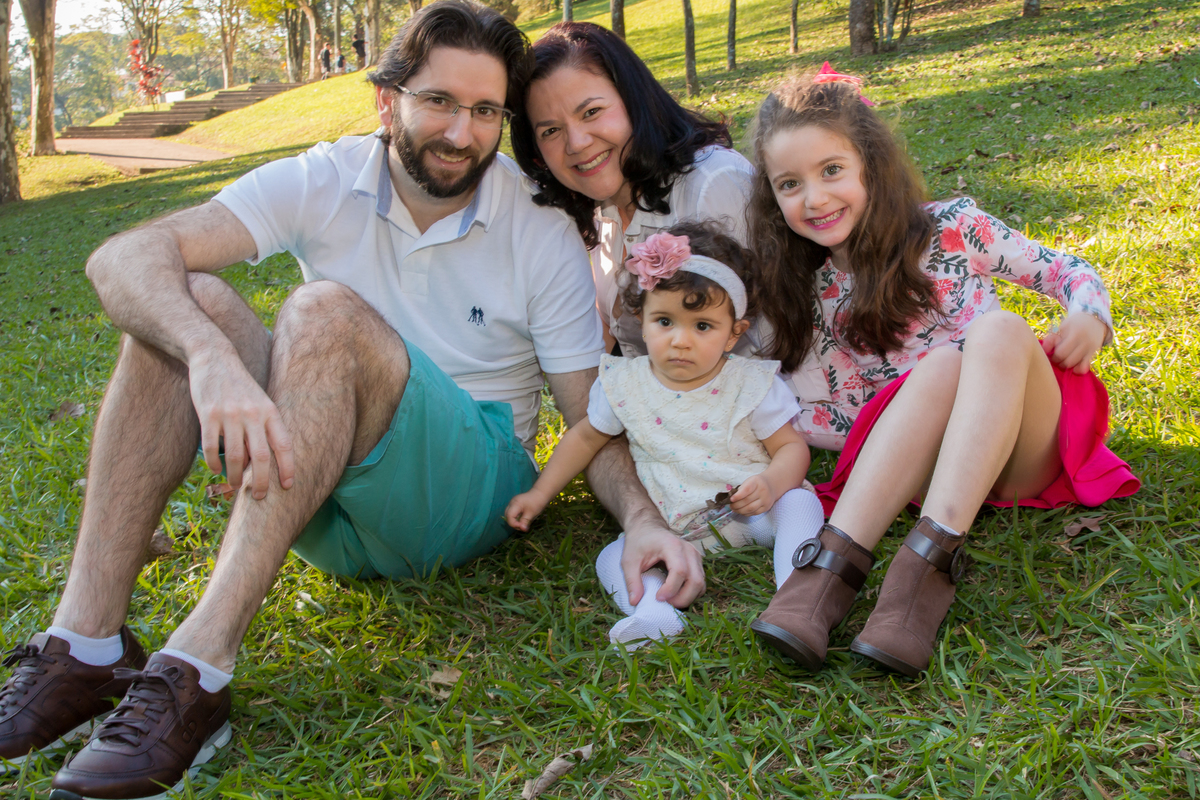 FOTOGRAFIA DE FAMÍLIA pai mãe e duas filhas SENTADOS NA GRAMA com ÁRVORES ao fundo no click da FOTÓGRAFA de ENSAIO SMASH THE FRUIT em SÃO PAULO, SP sorridentes em uma imagem colorida 