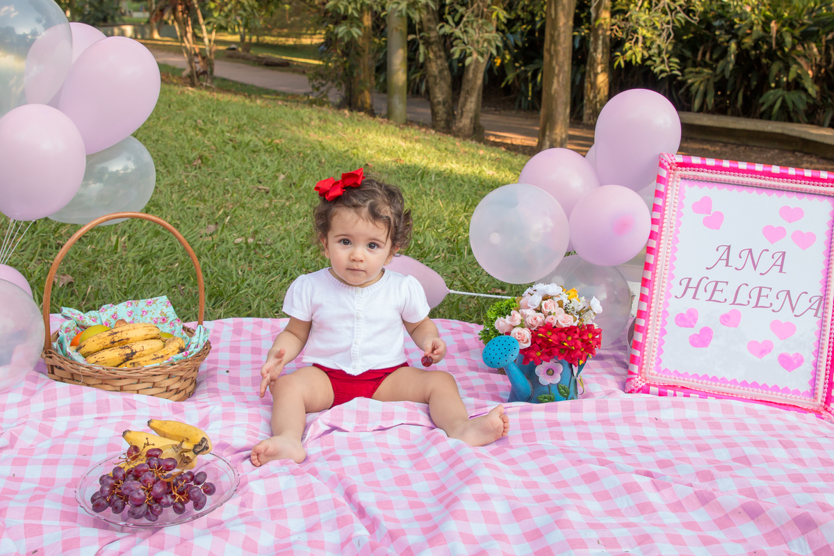 MENINA com LAÇO VERMELHO na cabeça sentada em uma toalha xadrez cor de rosa no click da FOTÓGRAFA de ENSAIO SMASH THE FRUIT em SÃO PAULO, SP sorridente em uma imagem colorida