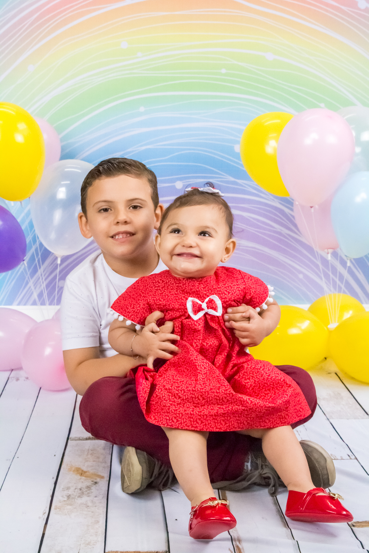 MENINA sentada de VESTIDO VERMELHO no colo do IRMÃO ele olhando para a CÂMERA no click da FOTÓGRAFA de ENSAIO SMASH THE CAKE em SÃO PAULO, SP sorridentes em uma imagem colorida