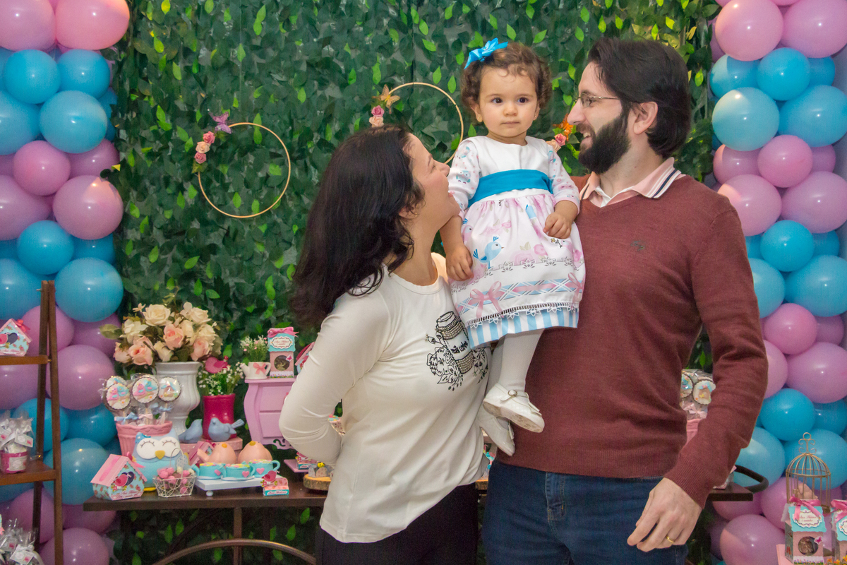 MENINA no colo dos PAIS de vestido com LAÇO AZUL em festa tema JARDIM ENCANTADO nas cores VERDE e CORES PASTÉIS no click da FOTÓGRAFA de FESTA INFANTIL em SÃO PAULO, SP em uma imagem colorida