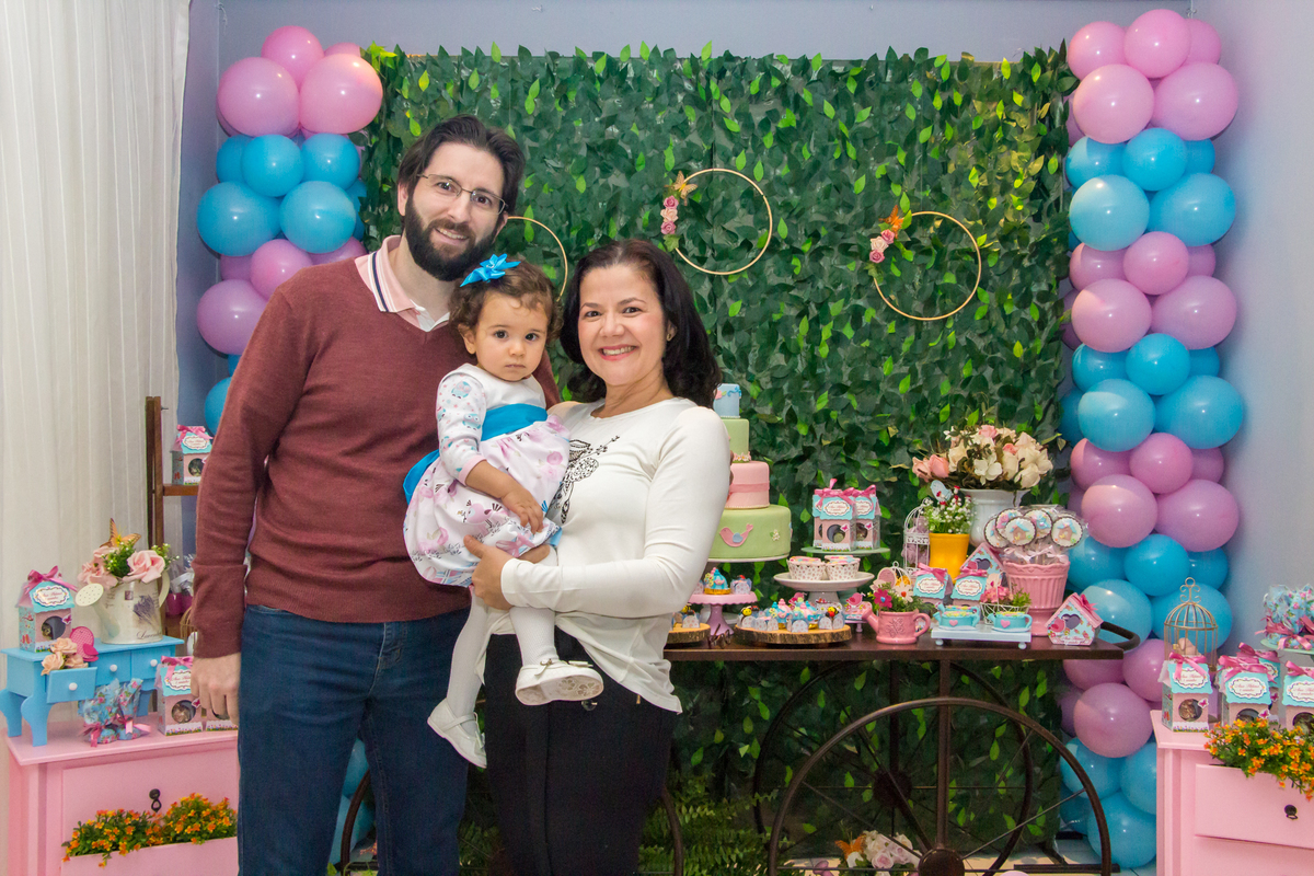 MENINA no colo dos PAIS de vestido com LAÇO AZUL em festa tema JARDIM ENCANTADO nas cores VERDE e CORES PASTÉIS no click da FOTÓGRAFA de FESTA INFANTIL em SÃO PAULO, SP em uma imagem colorida
