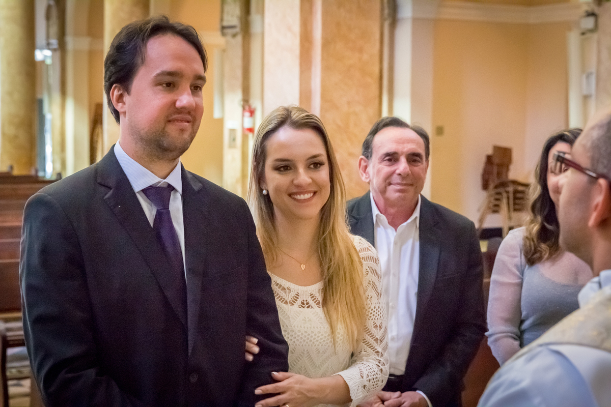 NOIVOS sorrindo para o PADRE  na IGREJA em CASAMENTO no click da FOTÓGRAFA de CASAMENTO em SÃO PAULO, SP em uma imagem colorida