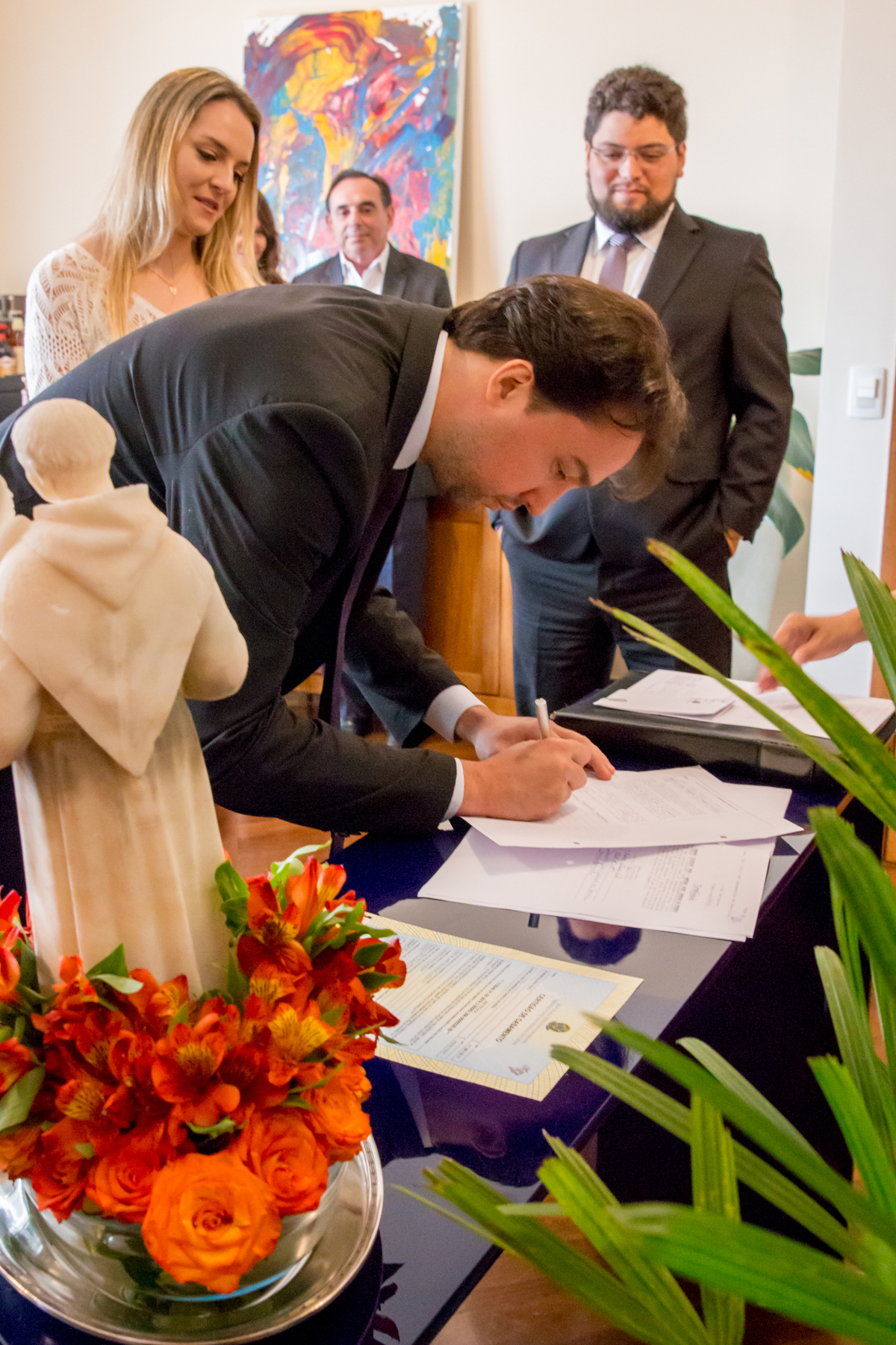 NOIVO assinando em CASAMENTO CIVIL com imagem de SANTO ANTÔNIO na mesa na casa dos NOIVOS no click da FOTÓGRAFA de CASAMENTO em SÃO PAULO, SP em uma imagem colorida