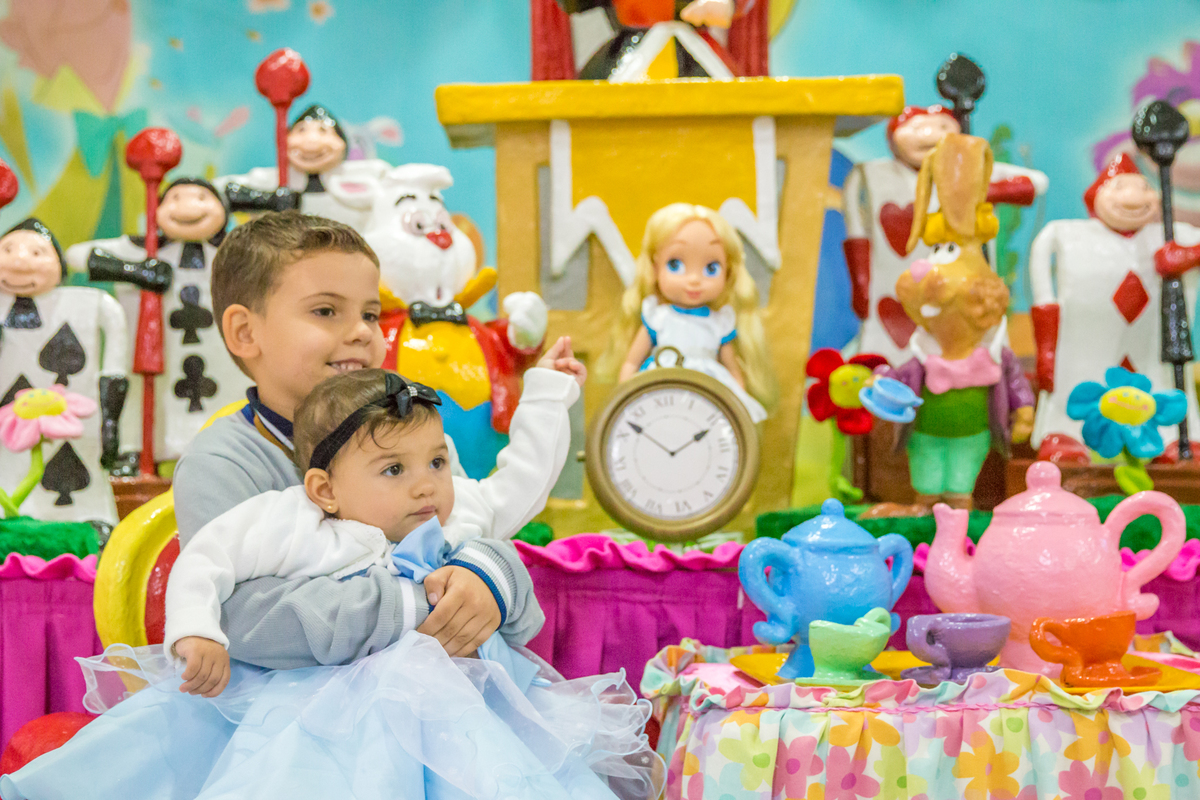 MENINA de VESTIDO AZUL e seu IRMÃO SENTADOS em frente a decoração tema ALICE NO PÁIS DAS MARAVILHAS no click do FOTÓGRAFO de FESTA INFANTIL em SÃO PAULO, SP em uma imagem colorida