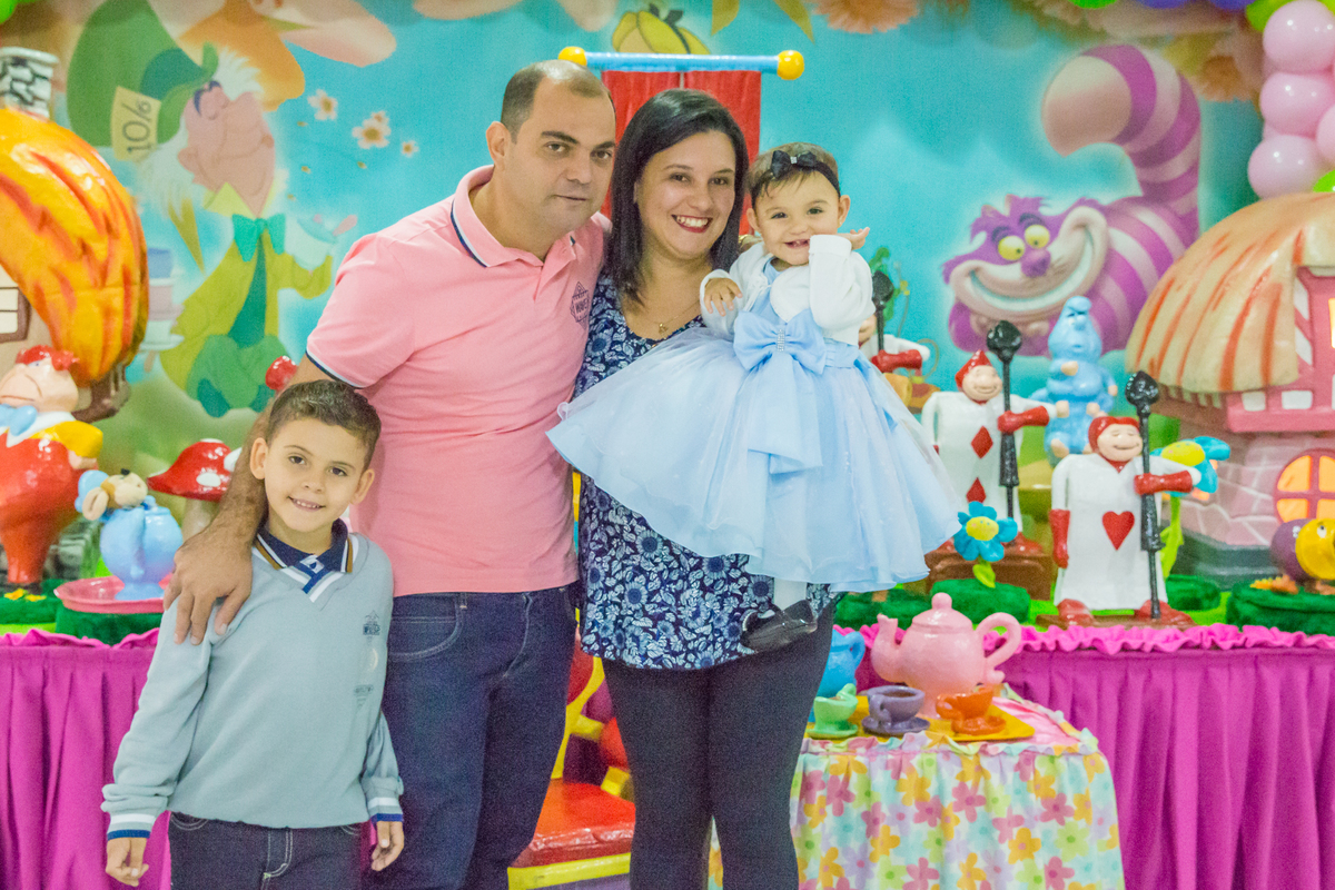 MENINA de VESTIDO AZUL e seu IRMÃO no COLO dos PAIS em frente a decoração tema ALICE NO PÁIS DAS MARAVILHAS no click do FOTÓGRAFO de FESTA INFANTIL em SÃO PAULO, SP em uma imagem colorida