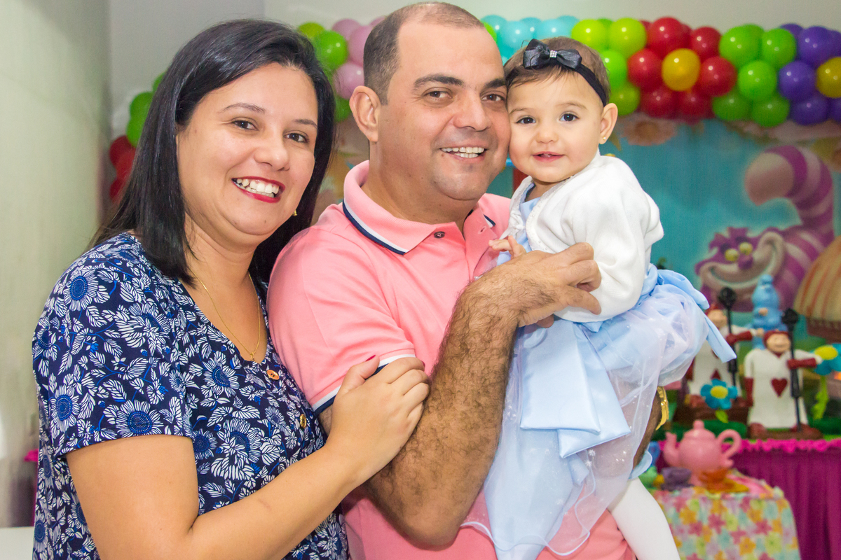 MENINA de VESTIDO AZUL no COLO dos PAIS em frente a decoração tema ALICE NO PÁIS DAS MARAVILHAS no click do FOTÓGRAFO de FESTA INFANTIL em SÃO PAULO, SP em uma imagem colorida