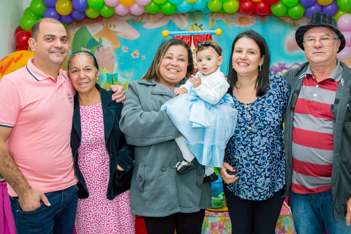 MENINA de VESTIDO AZUL no COLO dos AVÓS em frente a decoração tema ALICE NO PÁIS DAS MARAVILHAS no click do FOTÓGRAFO de FESTA INFANTIL em SÃO PAULO, SP em uma imagem colorida