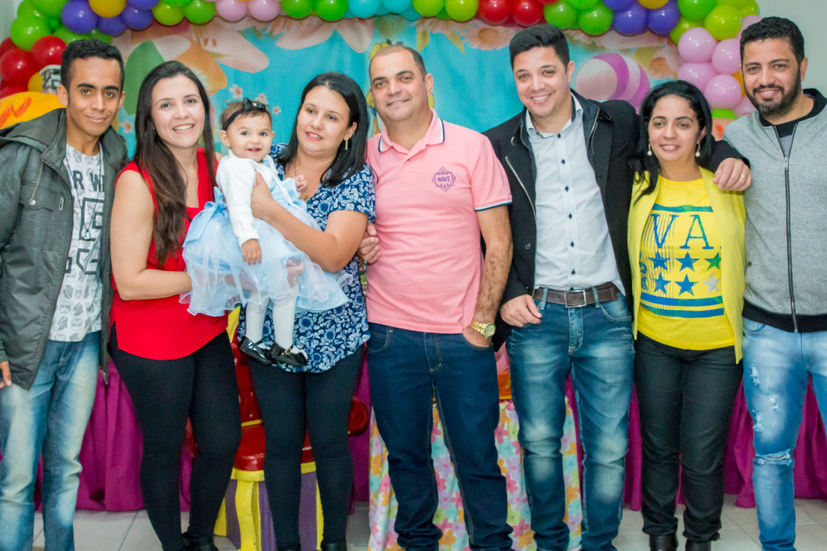 MENINA de VESTIDO AZUL no COLO dos TIOS em frente a decoração tema ALICE NO PÁIS DAS MARAVILHAS no click do FOTÓGRAFO de FESTA INFANTIL em SÃO PAULO, SP em uma imagem colorida