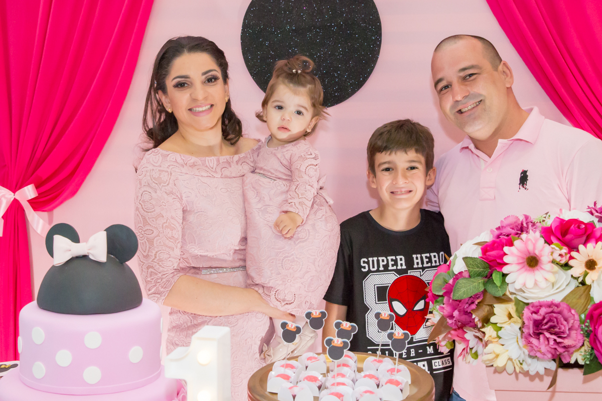 MENINA com os PAIS e IRMÃO de VESTIDO rosa em frente a decoração tema MINNIE nas cores ROSA e BRANCO no click do FOTÓGRAFO de FESTA INFANTIL em SÃO PAULO, SP em uma imagem colorida