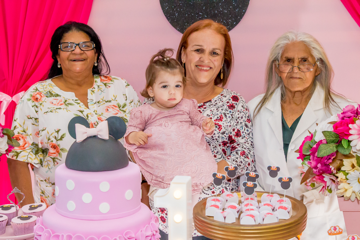 MENINA com as AVÓS de VESTIDO rosa em frente a decoração tema MINNIE nas cores ROSA e BRANCO no click do FOTÓGRAFO de FESTA INFANTIL em SÃO PAULO, SP em uma imagem colorida
