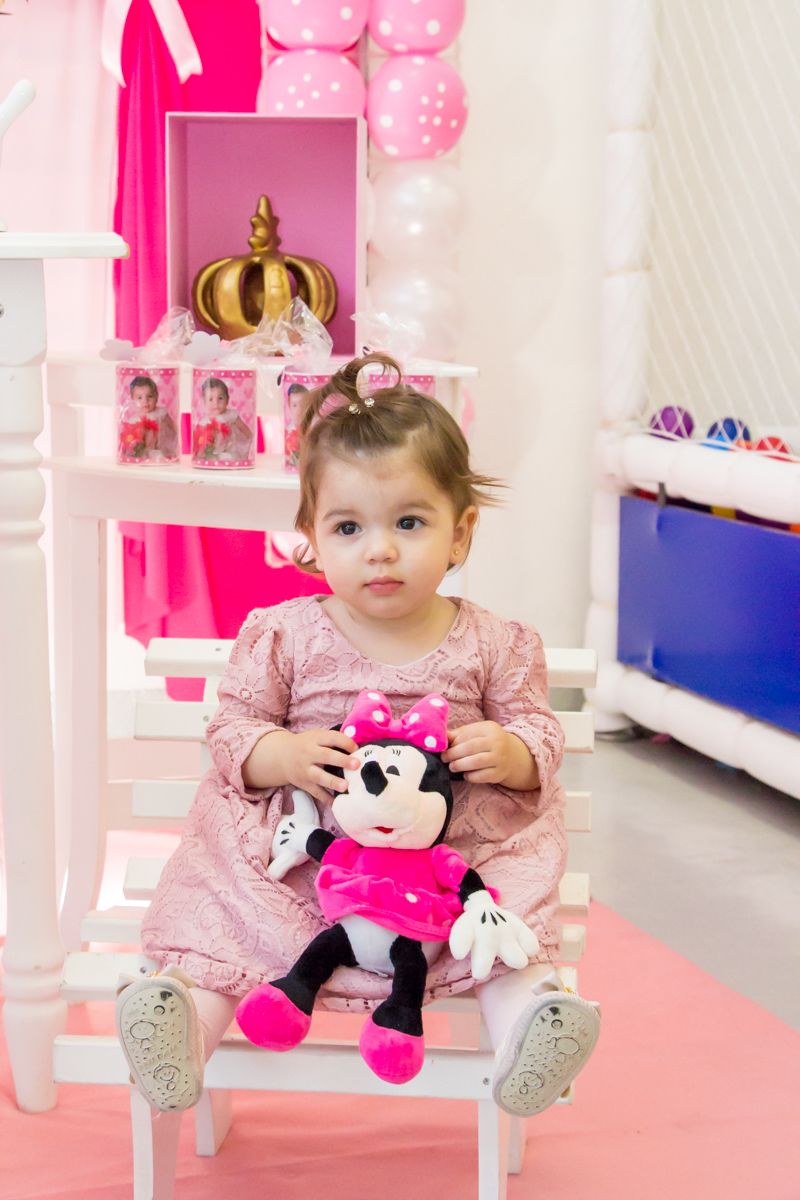 MENINA sentada de VESTIDO rosa em frente a decoração tema MINNIE nas cores ROSA e BRANCO no click do FOTÓGRAFO de FESTA INFANTIL em SÃO PAULO, SP em uma imagem colorida