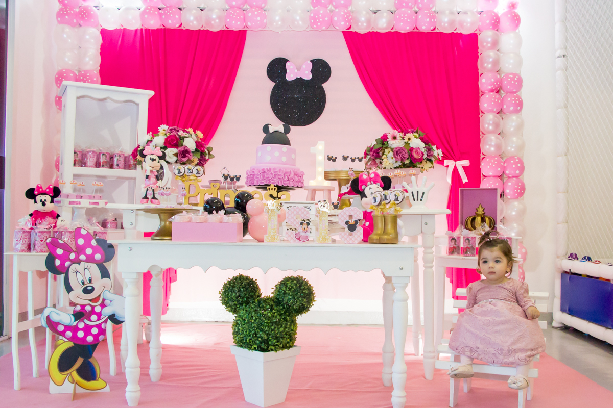MENINA sentada de VESTIDO rosa em frente a decoração tema MINNIE nas cores ROSA e BRANCO no click do FOTÓGRAFO de FESTA INFANTIL em SÃO PAULO, SP em uma imagem colorida