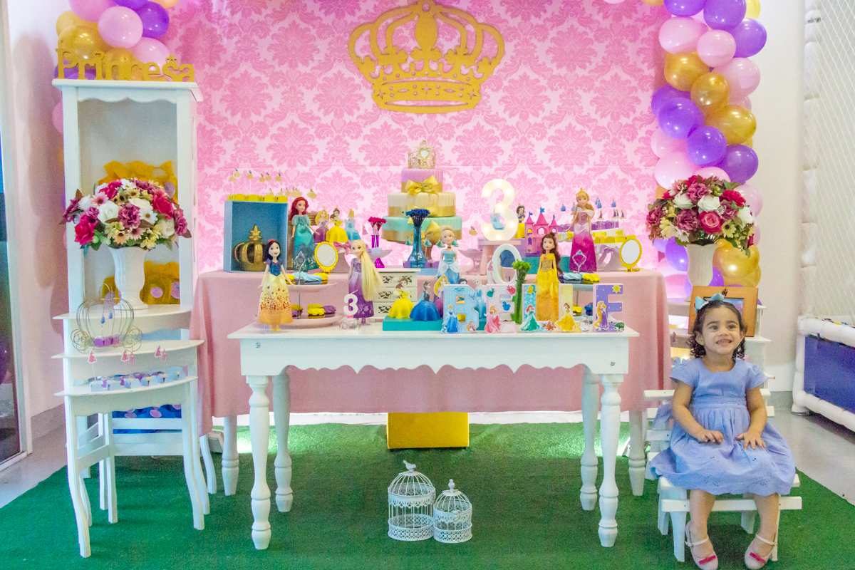 MENINA sorrindo de VESTIDO AZUL sentada em frente a decoração tema PRINCESAS nas cores ROSA, DOURADO e LILÁS no click do FOTÓGRAFO de FESTA INFANTIL em SÃO PAULO, SP em uma imagem colorida