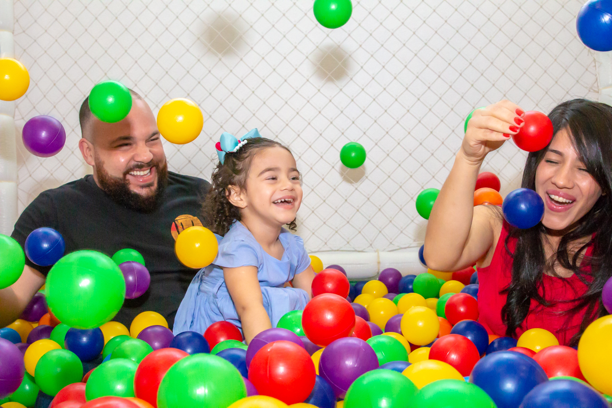 MENINA sorrindo de VESTIDO AZUL brincando com os PAIS em PISCINA de BOLINHAS no click do FOTÓGRAFO de FESTA INFANTIL em SÃO PAULO, SP em uma imagem colorida