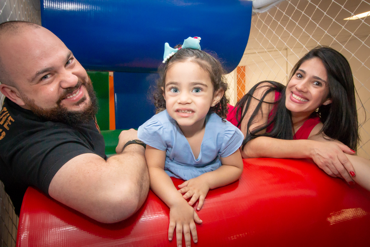 MENINA sorrindo de VESTIDO AZUL brincando com os PAIS em BRINQUEDÃO no click do FOTÓGRAFO de FESTA INFANTIL em SÃO PAULO, SP em uma imagem colorida