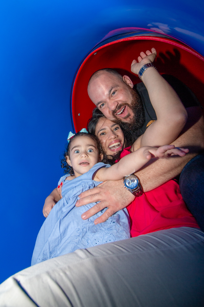 MENINA sorrindo de VESTIDO AZUL brincando com os PAIS em BRINQUEDÃO no click do FOTÓGRAFO de FESTA INFANTIL em SÃO PAULO, SP em uma imagem colorida