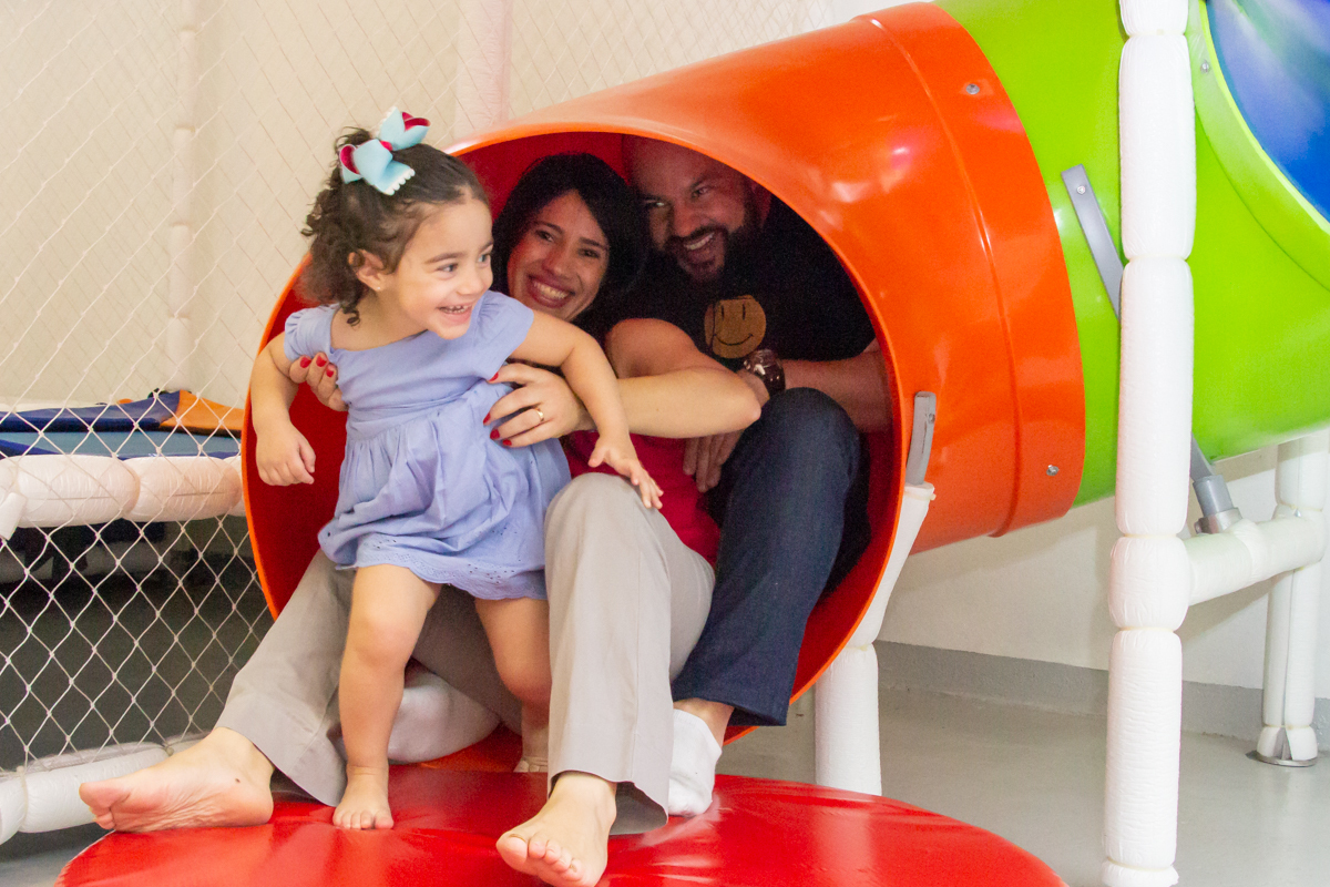 MENINA sorrindo de VESTIDO AZUL brincando com os PAIS em BRINQUEDÃO no click do FOTÓGRAFO de FESTA INFANTIL em SÃO PAULO, SP em uma imagem colorida