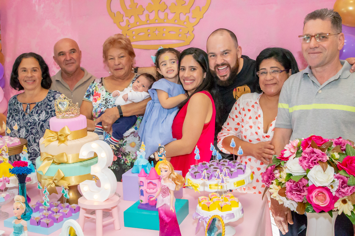 MENINA sorrindo de VESTIDO AZUL abraçada com os PAIS e AVÓS em frente a decoração tema PRINCESAS nas cores ROSA, DOURADO e LILÁS no click do FOTÓGRAFO de FESTA INFANTIL em SÃO PAULO, SP em uma imagem colorida