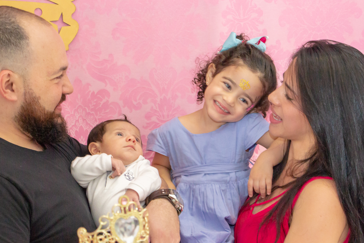 MENINA sorrindo de VESTIDO AZUL abraçada com os PAIS e IRMÃO em frente a decoração tema PRINCESAS nas cores ROSA, DOURADO e LILÁS no click do FOTÓGRAFO de FESTA INFANTIL em SÃO PAULO, SP em uma imagem colorida