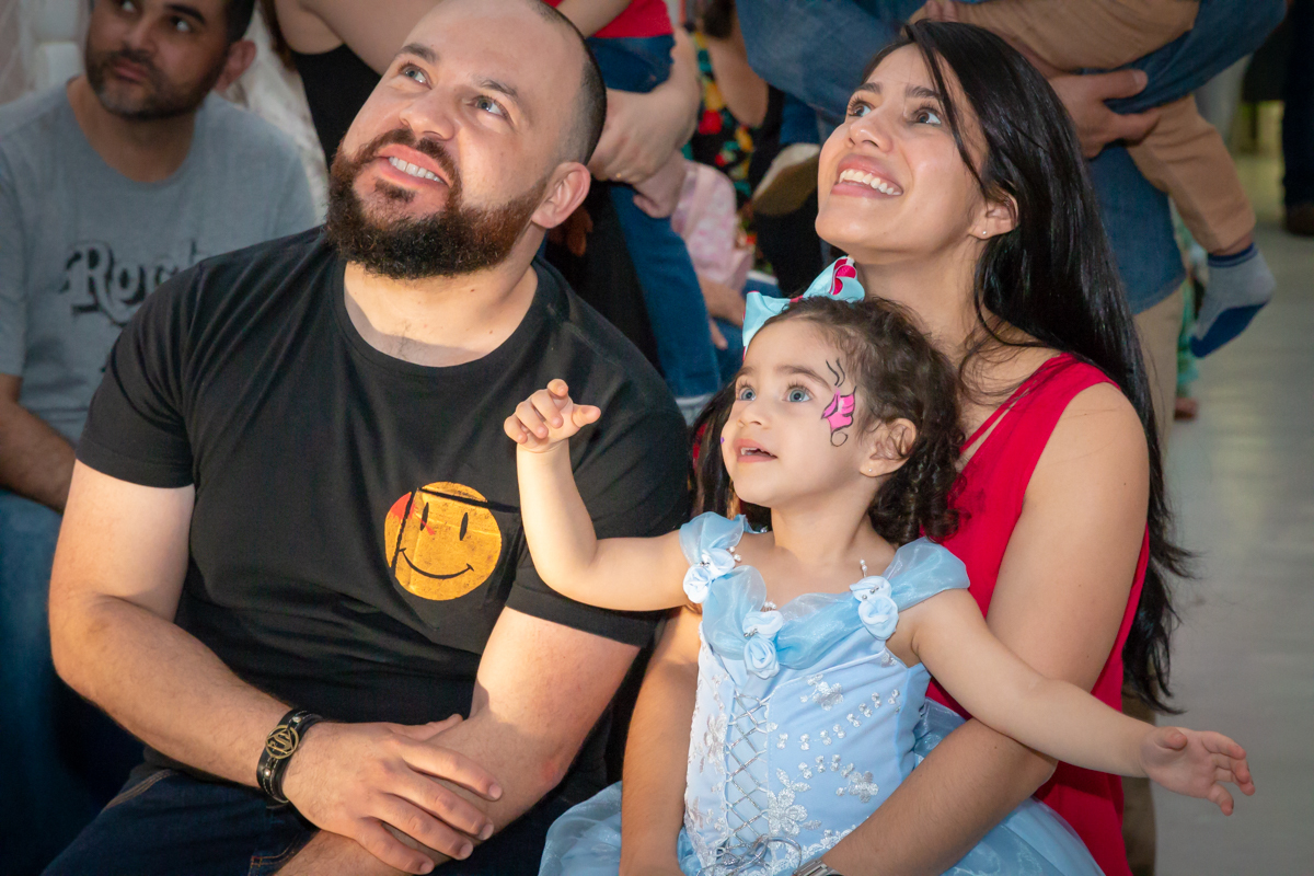 MENINA sorrindo de VESTIDO AZUL abraçada com os PAIS em frente a decoração tema PRINCESAS nas cores ROSA, DOURADO e LILÁS no click do FOTÓGRAFO de FESTA INFANTIL em SÃO PAULO, SP em uma imagem colorida