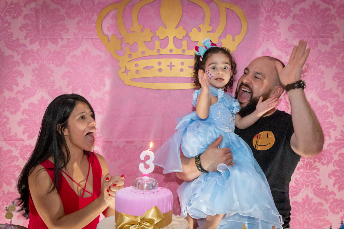 MENINA cantando PARABÉNS com os PAIS sorrindo de VESTIDO AZUL em decoração tema PRINCESAS nas cores ROSA, DOURADO e LILÁS no click do FOTÓGRAFO de FESTA INFANTIL em SÃO PAULO, SP em uma imagem colorida