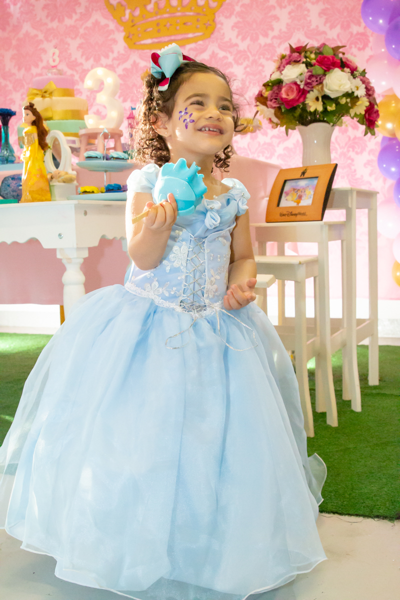 MENINA sorrindo de VESTIDO AZUL sentada em frente a decoração tema PRINCESAS nas cores ROSA, DOURADO e LILÁS no click do FOTÓGRAFO de FESTA INFANTIL em SÃO PAULO, SP em uma imagem colorida