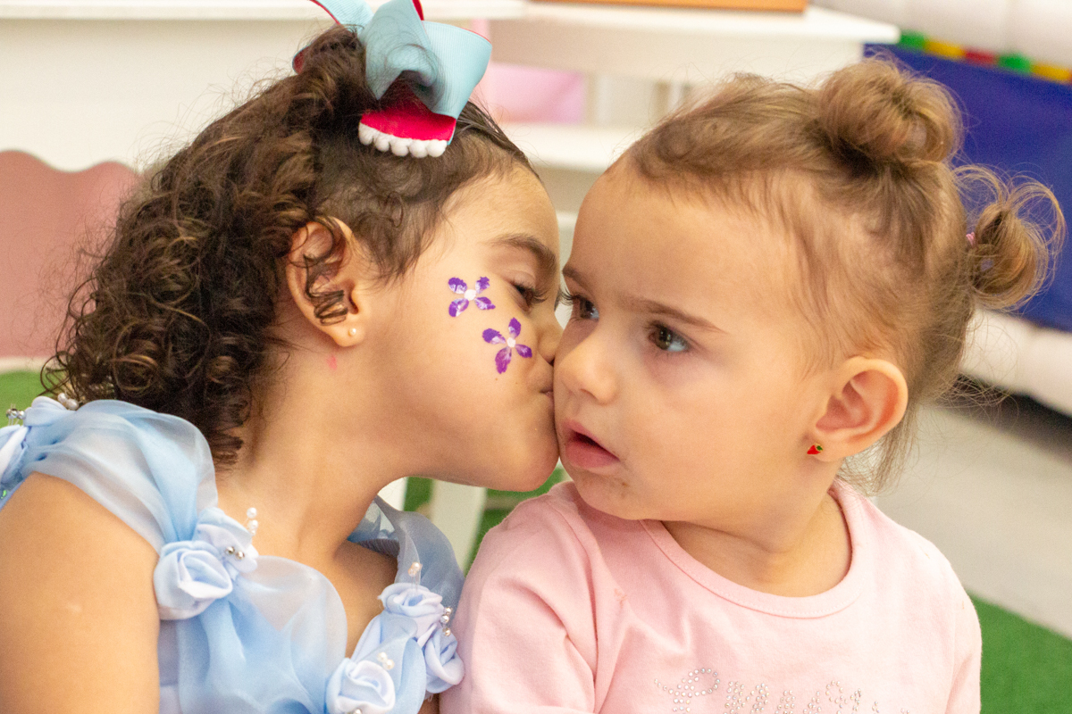 MENINA beijando a PRIMA sentadas em frente a decoração tema PRINCESAS nas cores ROSA, DOURADO e LILÁS no click do FOTÓGRAFO de FESTA INFANTIL em SÃO PAULO, SP em uma imagem colorida