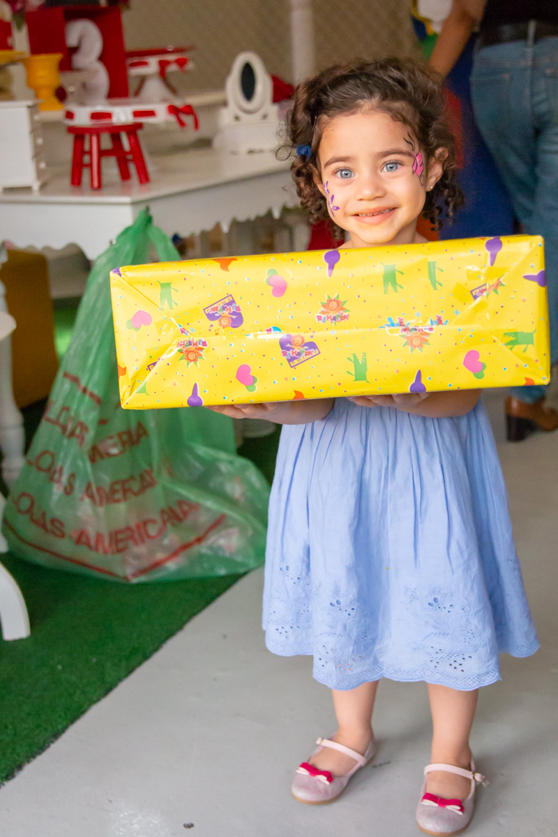 MENINA sorrindo de VESTIDO AZUL segurando o PRESENTE em frente a decoração tema PRINCESAS nas cores ROSA, DOURADO e LILÁS no click do FOTÓGRAFO de FESTA INFANTIL em SÃO PAULO, SP em uma imagem colorida