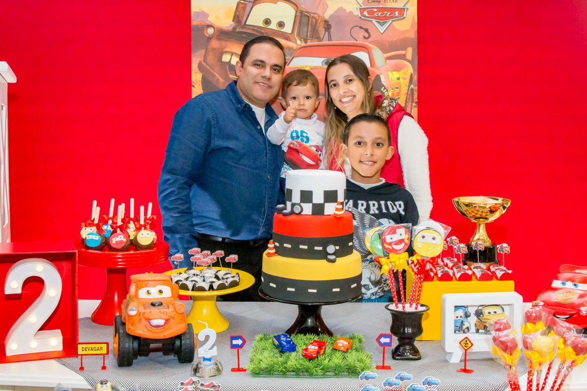 MENINO com sua FAMÍLIA posando em frente a decoração tema CARROS da DISNEY na cor VERMELHO no click do FOTÓGRAFO de FESTA INFANTIL em SÃO PAULO, SP em uma imagem colorida