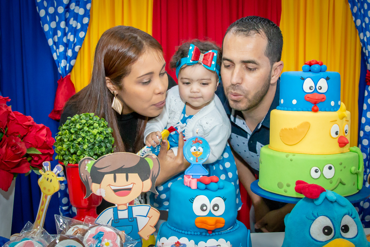 MENINA com seus PAIS assoprando a VELA cantando PARABÉNS em decoração tema GALINHA PINTADINHA no click do FOTÓGRAFO de FESTA INFANTIL em SÃO PAULO, SP em uma imagem colorida