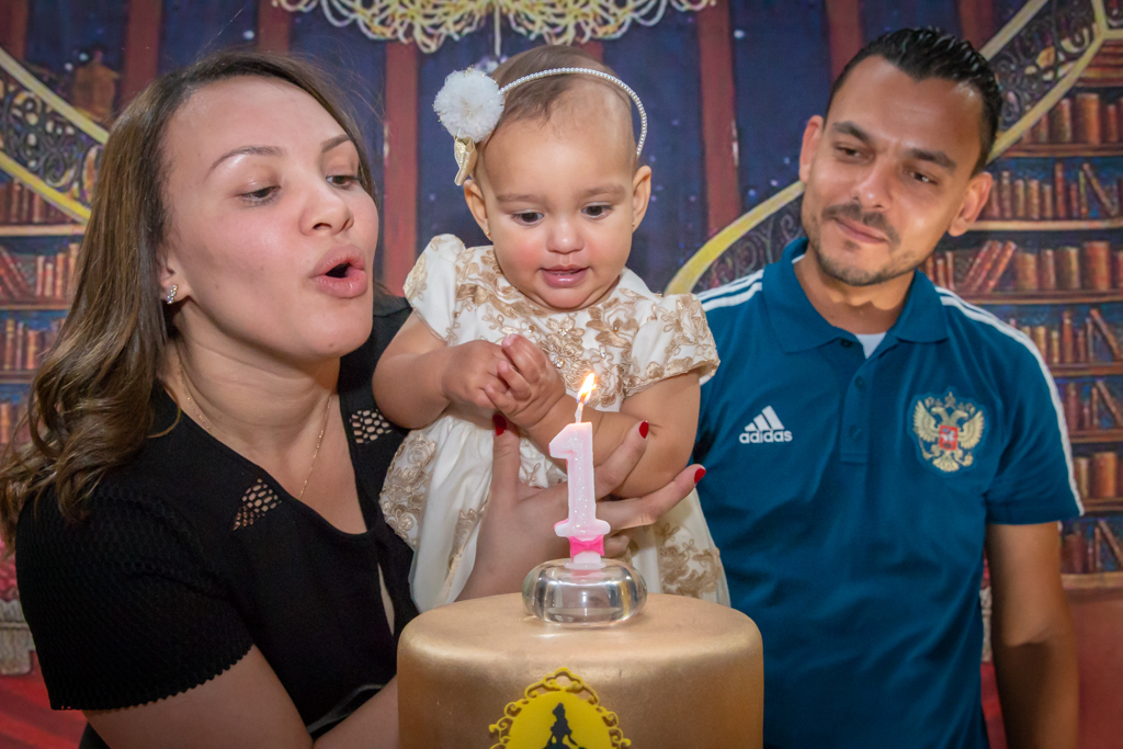 MENINA com seus PAIS cantando PARABÉNS assoprando VELINHA em frente a decoração tema a BELA e a FERA no click do FOTÓGRAFO de FESTA INFANTIL em SÃO PAULO, SP em uma imagem colorida