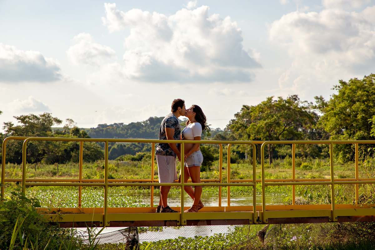 Mulher GRÁVIDA com a BARRIGA de fora, posando com o MARIDO em ENSAIO GESTANTE em um SÍTIO, em click do FOTÓGRAFO de GESTANTE.
