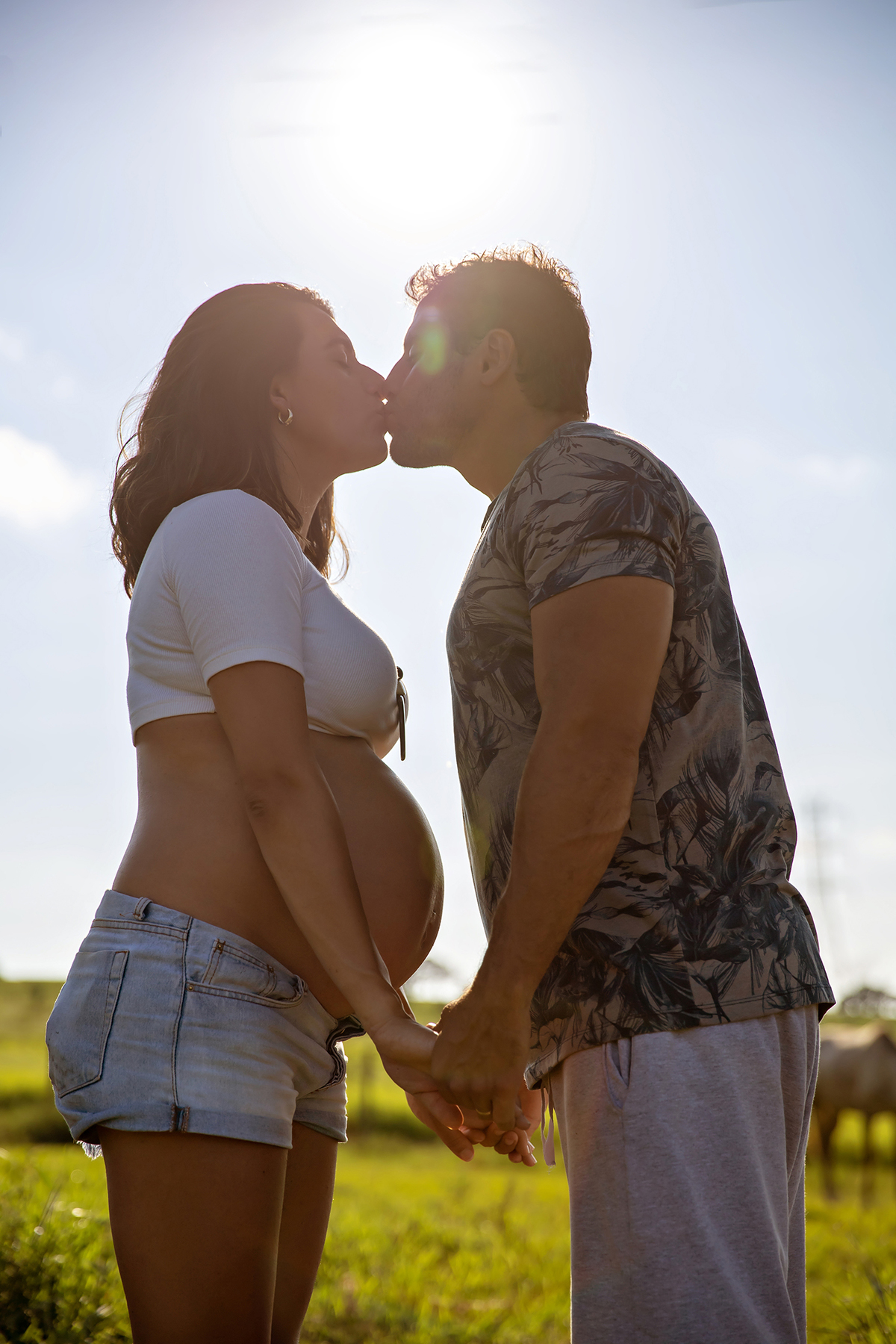 Mulher GRÁVIDA com a BARRIGA de fora, posando com o MARIDO em ENSAIO GESTANTE em um SÍTIO, em click do FOTÓGRAFO de GESTANTE.