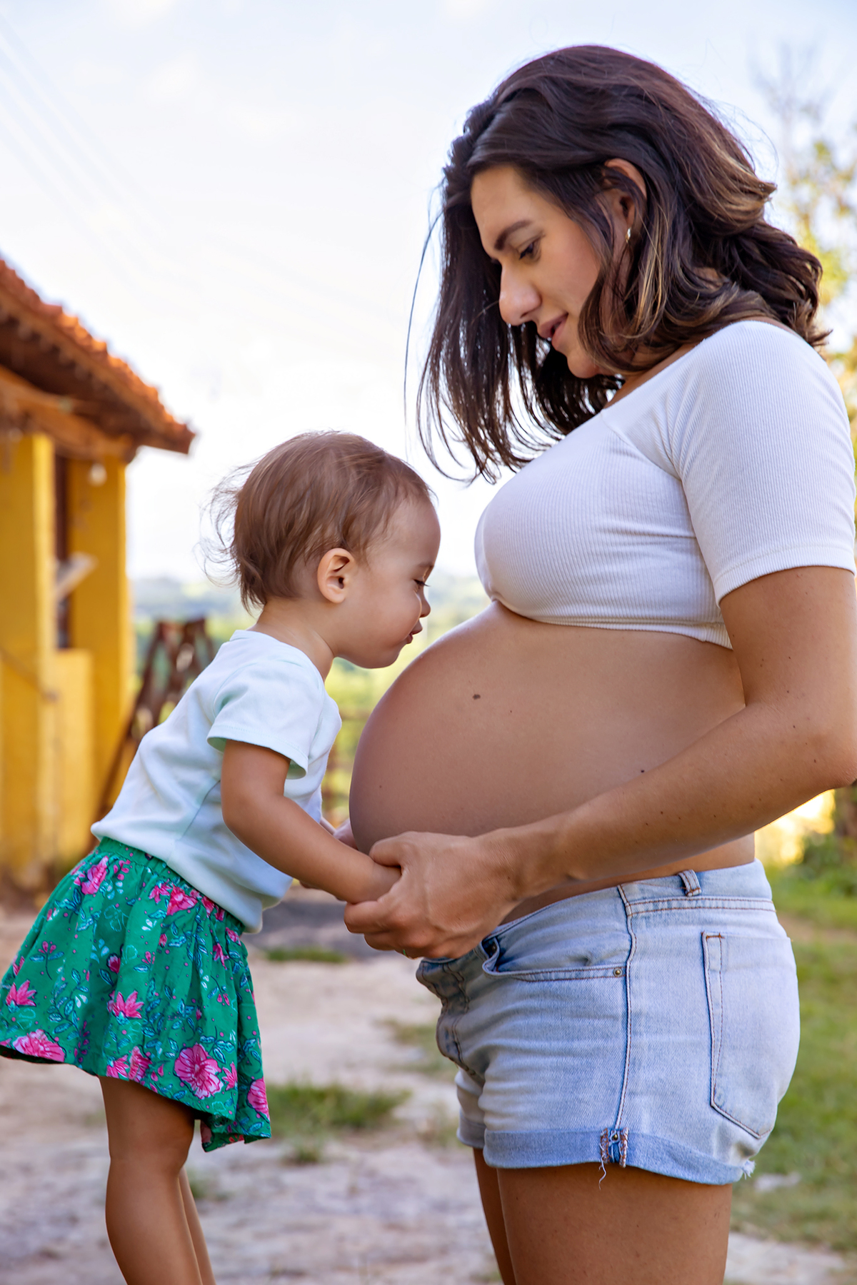 Mulher GRÁVIDA com a BARRIGA de fora, posando em ENSAIO GESTANTE com a FILHA em um SÍTIO, em click do FOTÓGRAFO de GESTANTE.