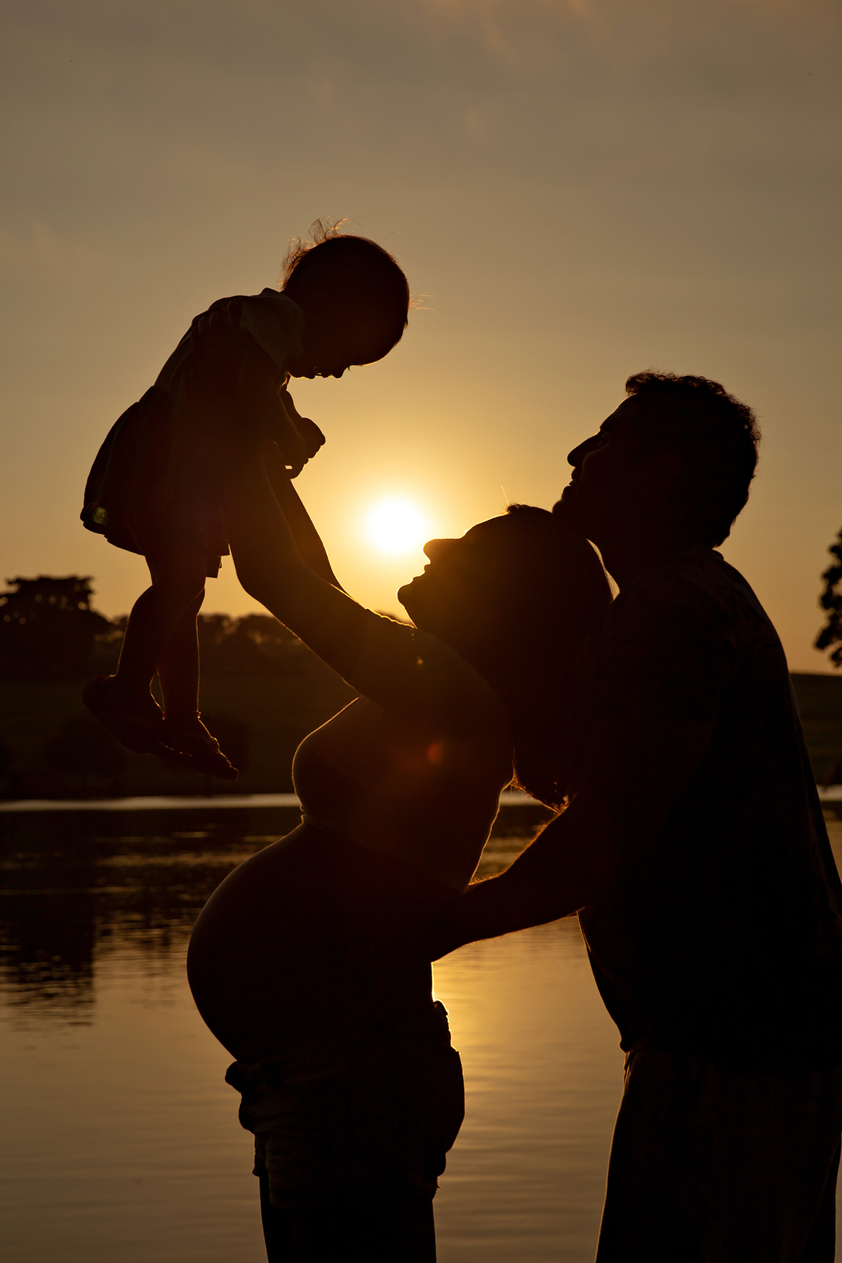 Mulher GRÁVIDA com a BARRIGA de fora, posando com o MARIDO e a FILHA em ENSAIO GESTANTE em um SÍTIO no POR do SOL, em click do FOTÓGRAFO de