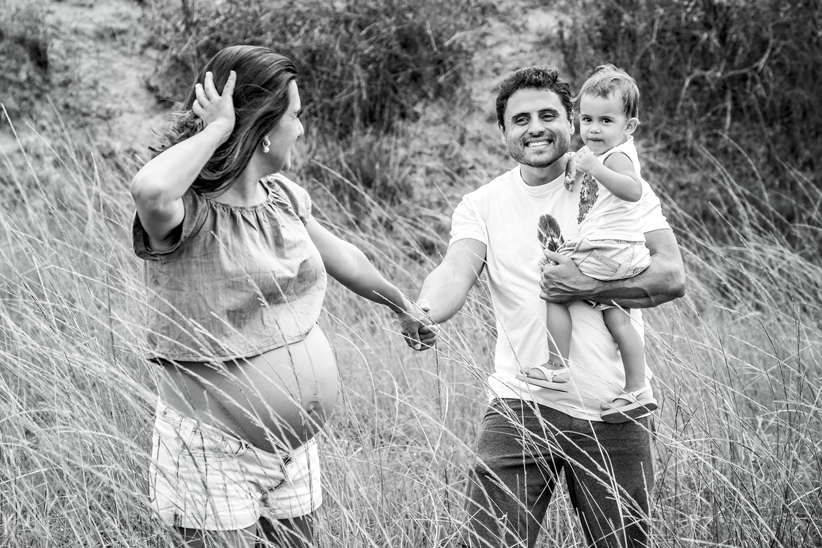 Mulher GRÁVIDA com a BARRIGA de fora, posando com o MARIDO e a FILHA em ENSAIO GESTANTE em um SÍTIO, em click do FOTÓGRAFO de GESTANTE.
