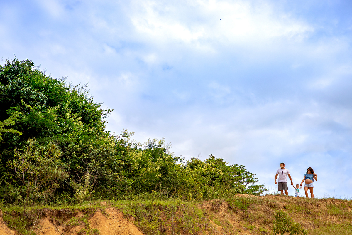 Mulher GRÁVIDA com a BARRIGA de fora, posando com o MARIDO e a FILHA em ENSAIO GESTANTE em um SÍTIO, em click do FOTÓGRAFO de GESTANTE.