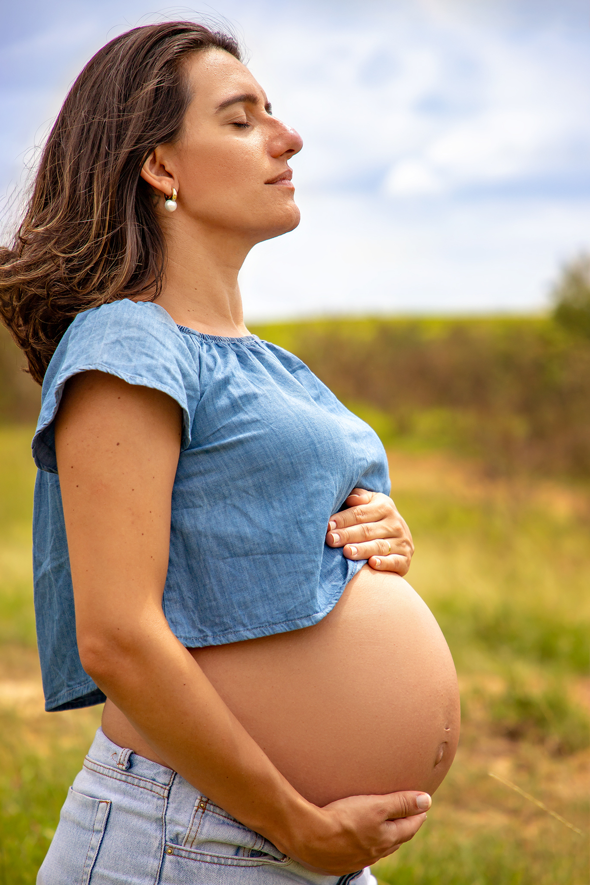 Mulher GRÁVIDA com a BARRIGA de fora, posando em ENSAIO GESTANTE em um SÍTIO, em click do FOTÓGRAFO de GESTANTE.