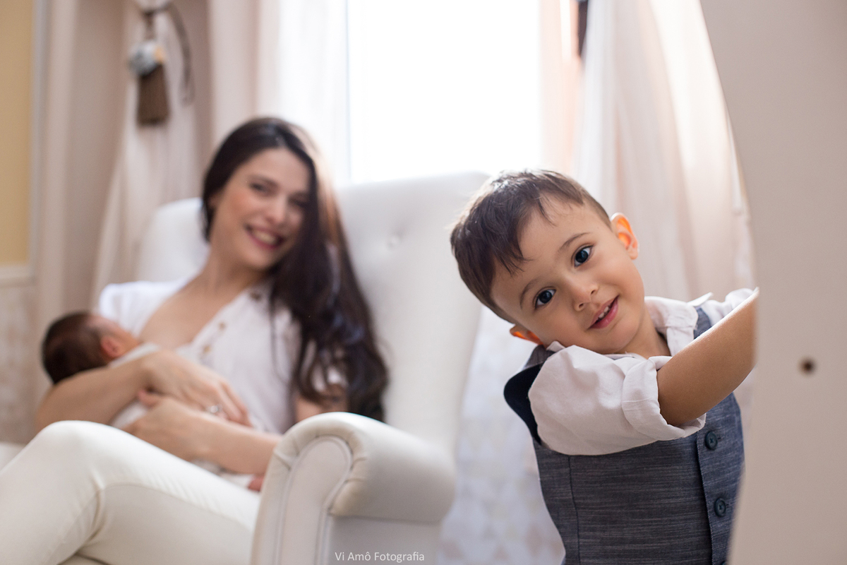 Ensaio newborn lifestyle do Gabriel 17 dias em casa, ensaio newborn a domicílio, Thali Freitas mamãe amamentando ao fundo o recem nascido Gabriel e irmão irmãozinho Gustavo na frente faento charme para a foto