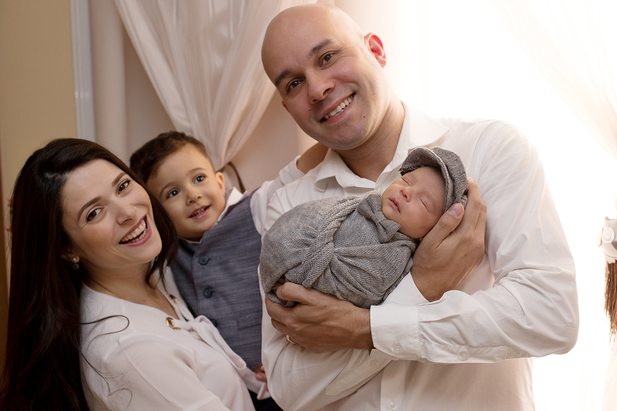 Foto em família em ensaio newborn em casa ensaio newborn lifestyle foto mãe, pai, irmão e recem nascido em tons branco e cinza ensaio a domicílio na Zona Sul de São Paulo