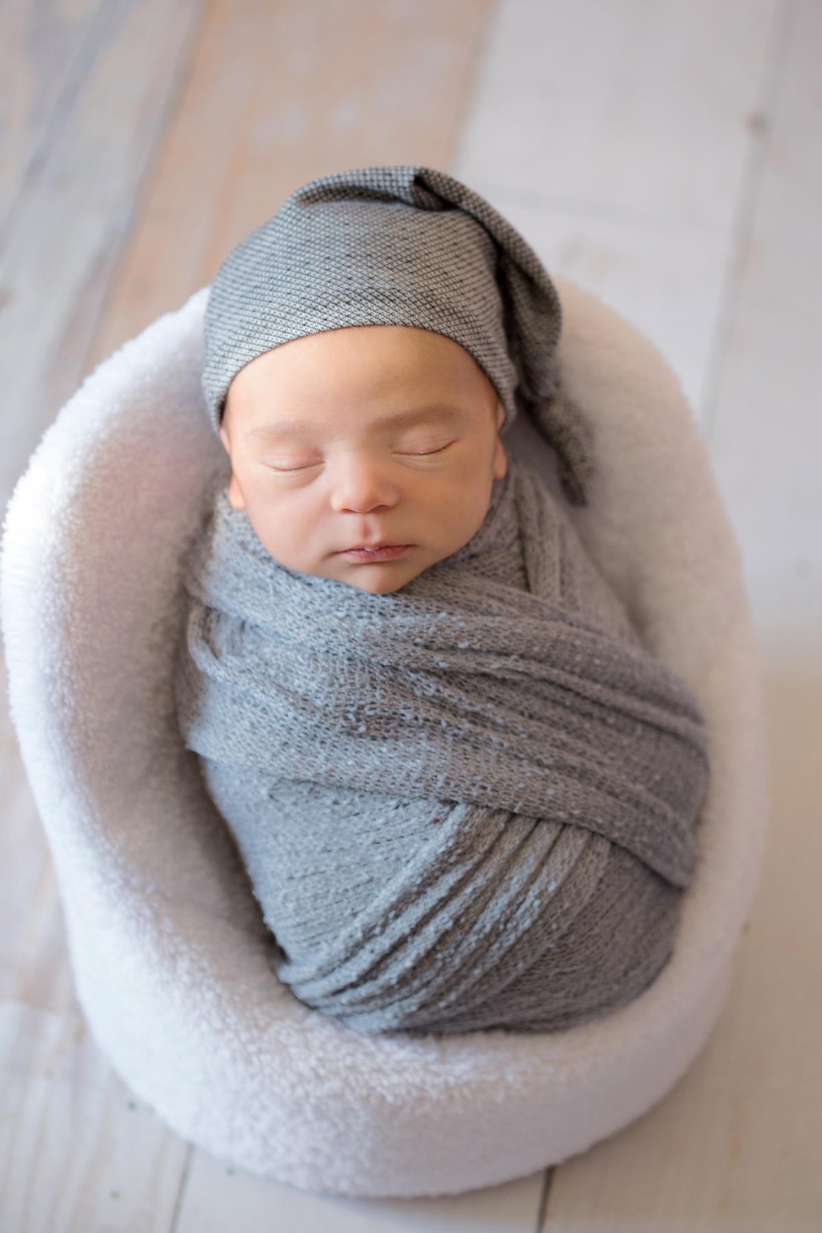 Bebê enroladinho em wrap cinzo com gorro cinza em mini poltrona ensaio newborn em casa ensaio newborn a domícilia Zona Sul e Zona Oeste de São Paulo