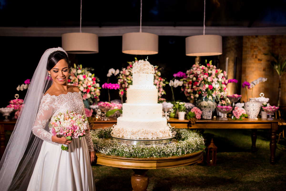 Noiva pousando para fotos com o buque e ao fundo o bolo do casamento
