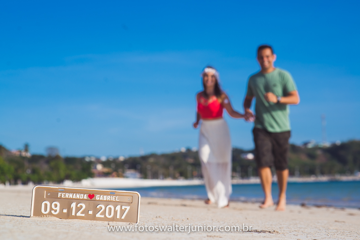 PLACA COM A DATA DO CASAMENTO COM O CASAL NO FUNDO FAZENDO AS FOTOS DO SEU ENSAIO PRÉ WEDDING NA PRAIA DE INEMA EM SALVADOR-BAHIA