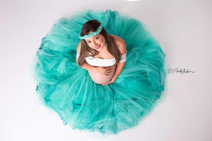 Foto de gestante de top branco e saia rodada verde no fundo branco