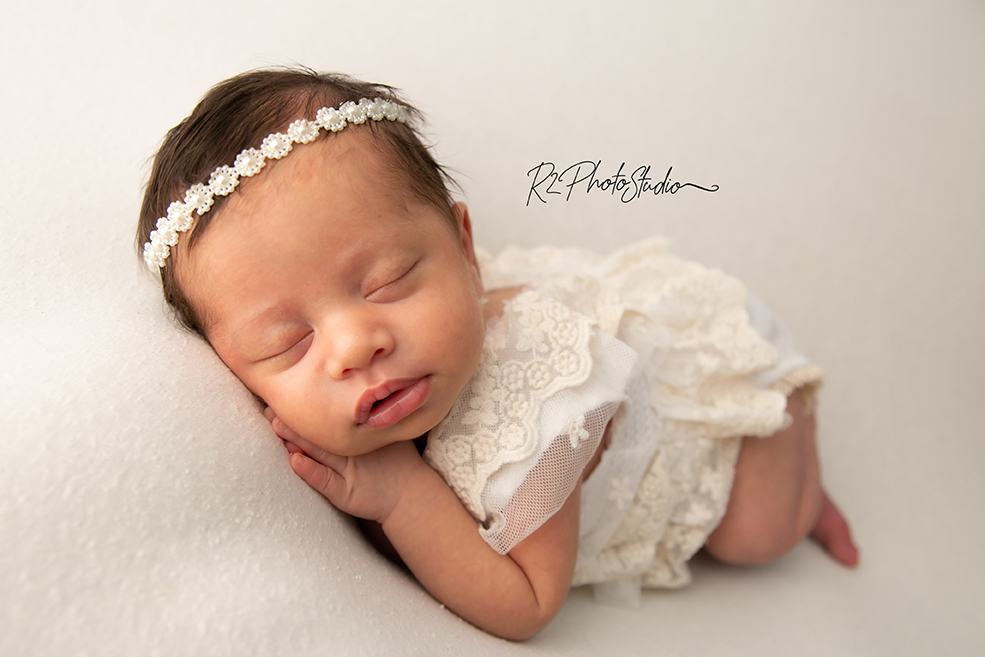 Foto de bebe menina vestida de renda e tiara de perolas deitada no puff